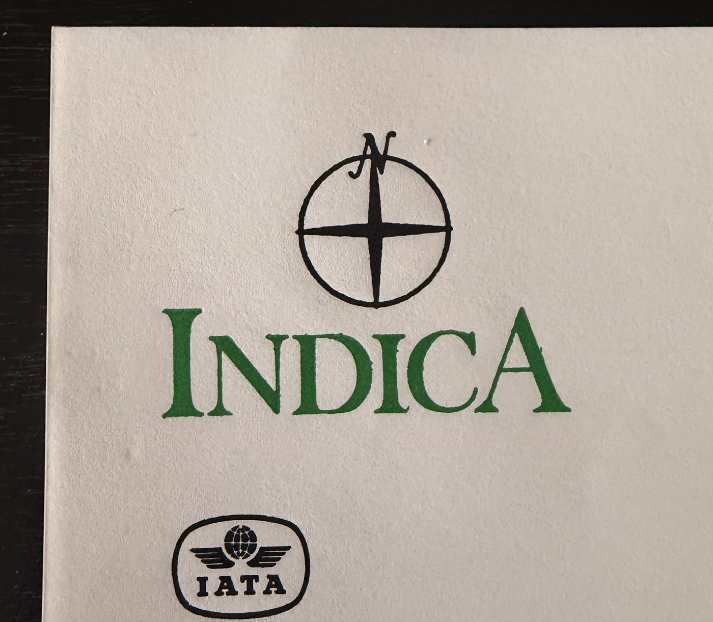 The original Indica logo: a compass rose with a stylized N marking north, above the word INDICA in green serif type, with an IATA badge below.